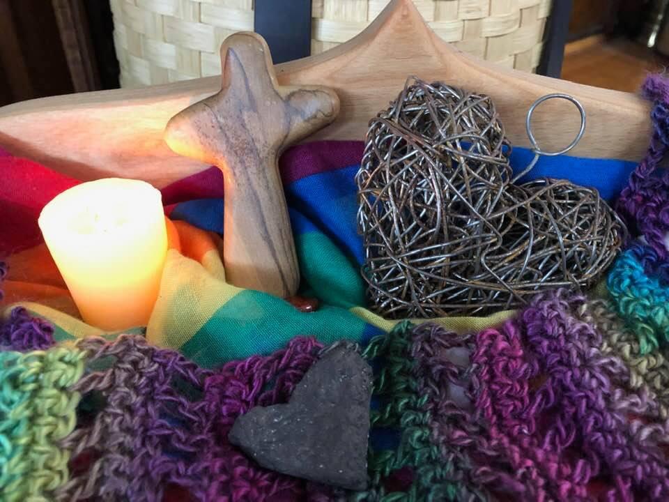 Lit candle with a cross and heart ornament wit a rainbow blanket.