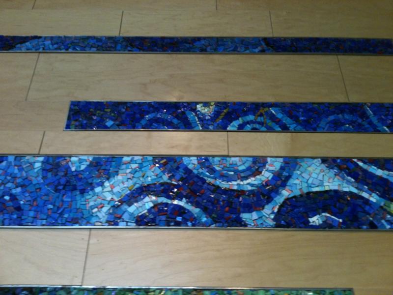 Mosaic displayed on wall, Mosaic tiles are different blues, placed in twirls.