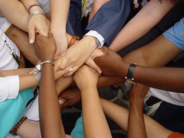 Hands of all race, gender, and age placing their hands into a pile in the middle of them.