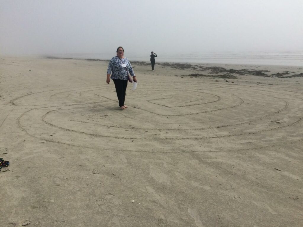 A woman walking a labyrinth made in the sand on a beach.